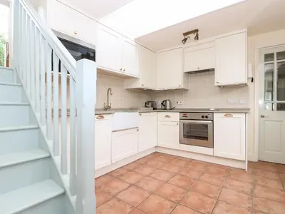 a kitchen with white cabinets and a staircase at Oreo's Cottage in St. Agnes