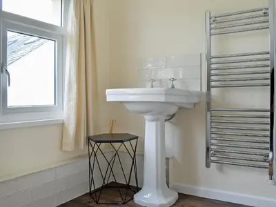 a bathroom with a white sink and a window at Littlewood in Saint Columb Major