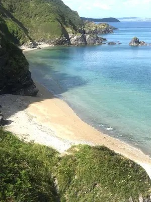 a beach with blue water and rocks in the ocean at Corner Cottage Mevagissey in Mevagissey