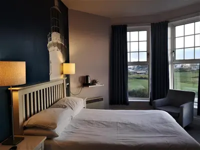 a bedroom with a bed and a chair and a lighthouse at Oceanside Lifestyle Hotel in Newquay