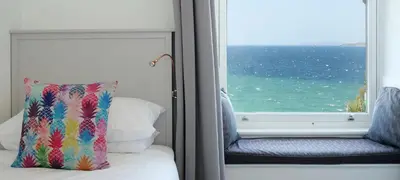 a bed with a pillow and a window with the ocean at Waves End, St Ives, Hot tub and Parking in St Ives