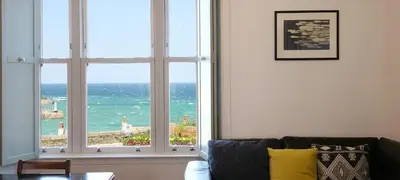 a living room with a large window looking out at the ocean at Waves End, St Ives, Hot tub and Parking in St Ives