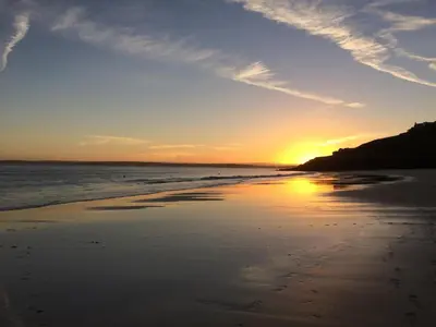 a sunset on a beach with footprints in the sand at Waves End, St Ives, Hot tub and Parking in St Ives