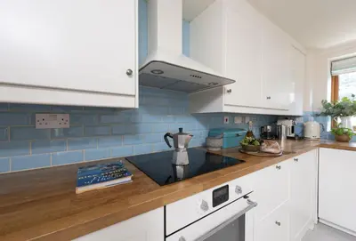 a kitchen with white cabinets and blue tiles at Curlew's Cwtch in Wadebridge
