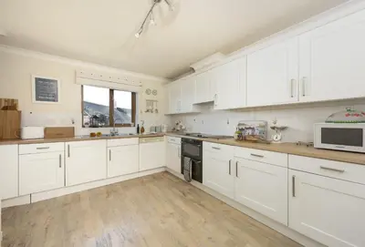 a large white kitchen with white cabinets and wooden floors at Keepers Cottage in Wadebridge