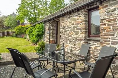 a patio with a table and chairs in front of a stone building at Little Gull in Polzeath