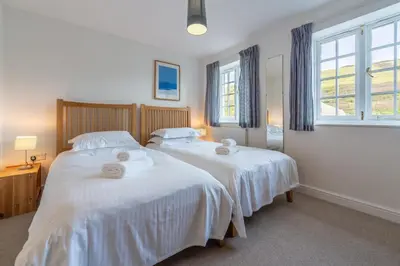 two beds in a bedroom with white sheets and windows at No2 The Fish Cellars in Port Isaac