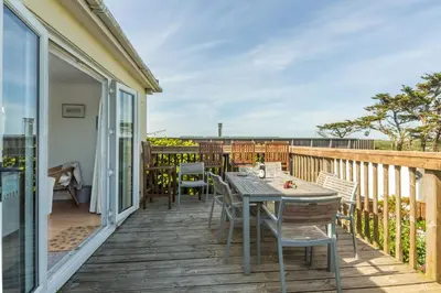 a patio with a table and chairs on a deck at Palm Trees in Polzeath