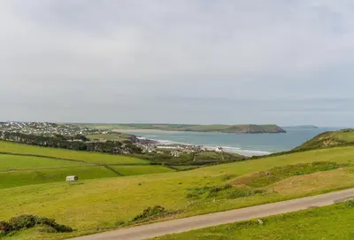 a road in the middle of a green field with the ocean at Pentewan in Polzeath