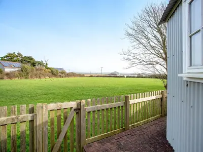 a wooden fence next to a field with a farm at Candles Cottage in Cubert