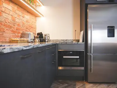 a kitchen with a stainless steel refrigerator and a brick wall at Padstow Escapes - The Long Room Luxury Apartment in Padstow