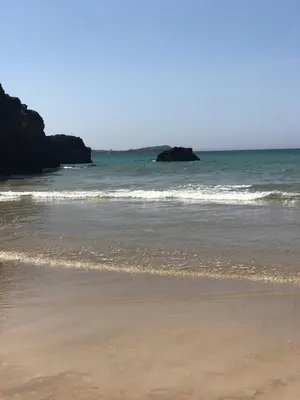 a beach with the ocean and a rock in the water at Beachy in Newquay