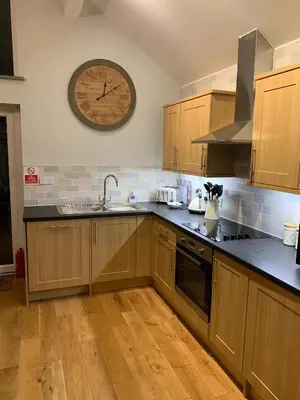 a kitchen with wooden cabinets and a clock on the wall at Bossiney Cove Cottage in Tintagel
