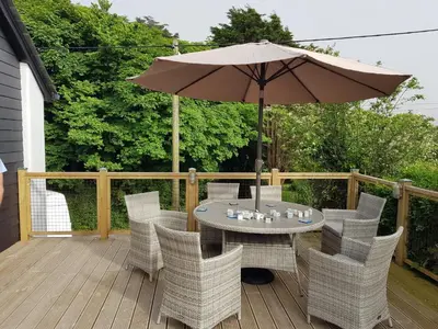 a table and chairs with an umbrella on a deck at Bossiney Cove Cottage in Tintagel