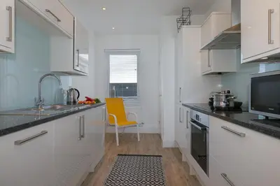 a kitchen with white cabinets and a yellow chair in it at SeaCrest 2 in St Ives