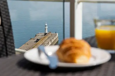 a plate of food on a table with a lighthouse at Marine Point, Mevagissey - sensational cliff top views of harbour and bay in Mevagissey