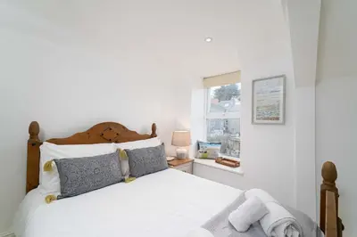 a bedroom with a bed with white sheets and a window at Shrimp Cottage in St Ives