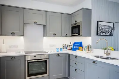 a kitchen with white cabinets and a sink at Seafarers, Mevagissey - Coastguard Cottage overlooking harbour in Mevagissey