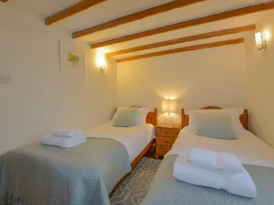 two beds in a room with wooden ceilings at Hook Cottage in Looe