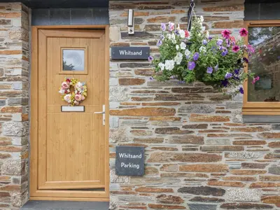 a stone house with a wooden door and flowers at Whitsand in Saltash