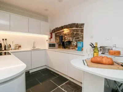 a kitchen with white cabinets and a counter with bread on a cutting board at Rock House in Tintagel
