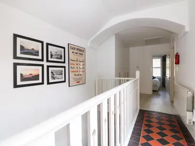 a hallway with a white staircase with pictures on the wall at Rock House in Tintagel