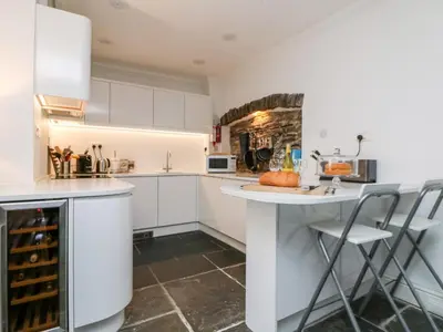 a kitchen with white cabinets and a counter and chairs at Rock House in Tintagel