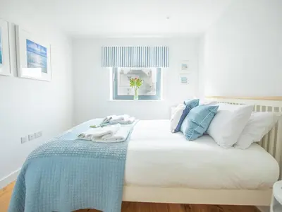 a white bedroom with a bed with blue and white pillows at Onshore 6 - Newquay Towan Beach View in Newquay