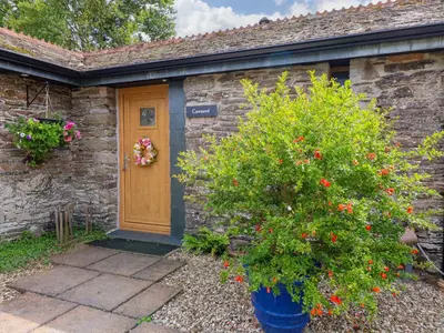a stone house with a wooden door and a bush at Cawsand in Saltash