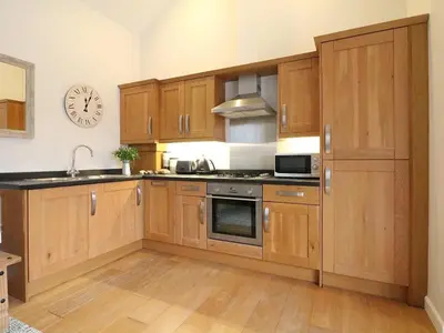 a kitchen with wooden cabinets and a clock on the wall at Hazel Barn in Falmouth