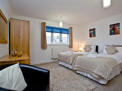 a bedroom with two beds and a desk and a window at Fistral View At Bredon Court in Newquay