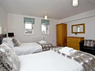 a bedroom with two beds and a dresser and two windows at Bredon Court, Poseidon Penthouse in Newquay