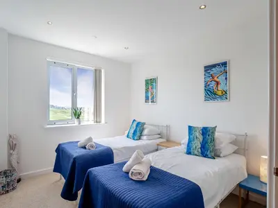 a bedroom with two beds with blue sheets and a window at 7 Cribbar in Newquay