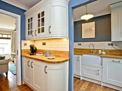 a kitchen with white cabinets and blue walls at Headland Views in Newquay