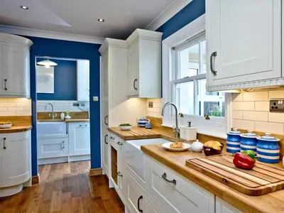 a kitchen with white cabinets and blue walls at Headland Views in Newquay