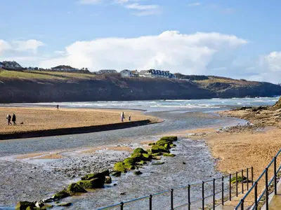 a beach with people walking on the sand and water at Quay House, Porth Beach in Newquay