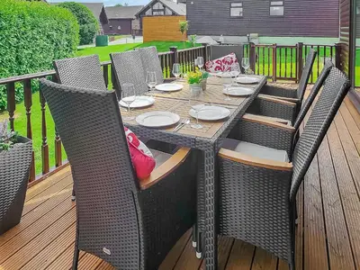 an outdoor table with wicker chairs on a deck at Beech Lodge - Retallack Resort in Saint Columb Major
