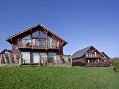 a large wooden house with a balcony on a green field at Beech Lodge - Retallack Resort in Saint Columb Major