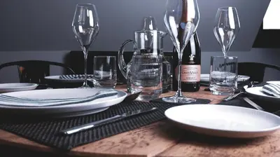 a wooden table with plates and glasses and a bottle of wine at Padstow Escapes - Pajar Luxury Penthouse Apartment in Padstow