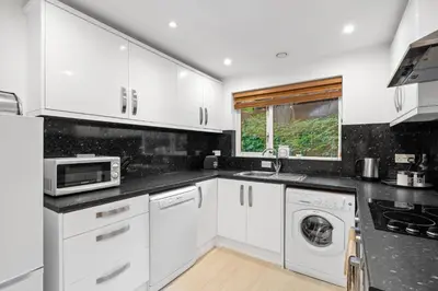 a kitchen with white cabinets and a washer and dryer at Tincroft Cottage - high end, luxury living near the beach in Truro