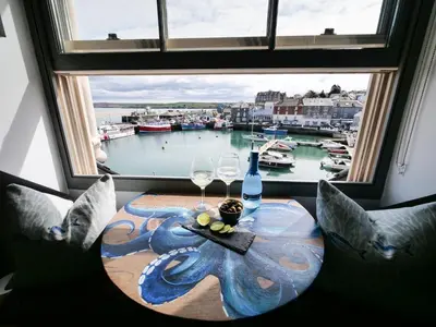 a table with wine glasses and a window with a view of a harbor at Padstow Escapes - Teyr Luxury Penthouse Apartment in Padstow