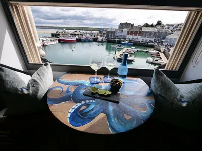 a table with two wine glasses and a view of a harbor at Padstow Escapes - Teyr Luxury Penthouse Apartment in Padstow