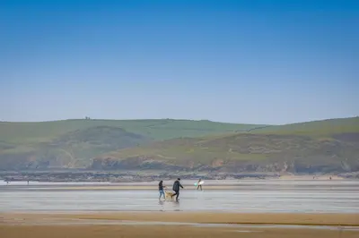three people and a dog walking on a beach at Westward 14 Polzeath in Polzeath