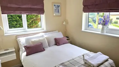 a bedroom with a white bed with two windows at Fairlee in Perranporth