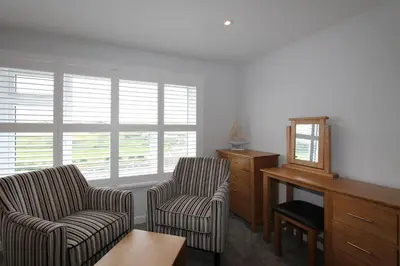 a living room with two chairs and a desk and windows at Mawgan Porth Apartments in Mawgan Porth
