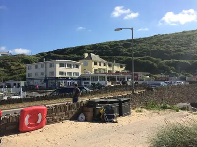 a man walking on a retaining wall near a beach at Mawgan Porth Apartments in Mawgan Porth