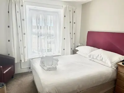 a bedroom with a white bed with a purple headboard and a window at King Arthurs Arms in Tintagel