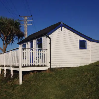 a white house with a porch and a palm tree at Hippy beach shack in Hayle