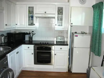 a kitchen with white cabinets and a stove and a refrigerator at Chalet 151, Perran Sands in Perranporth