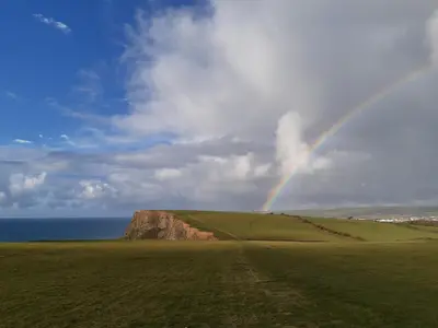 a rainbow over a field with the ocean at Chalet 18 Widemouth Bay Holiday Village in Bude